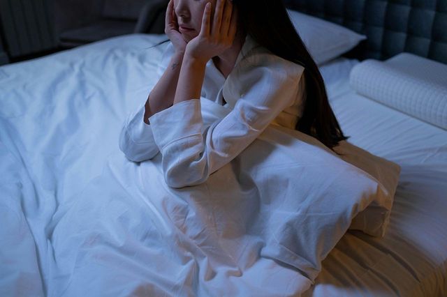Woman sits up in bed with head in her palms