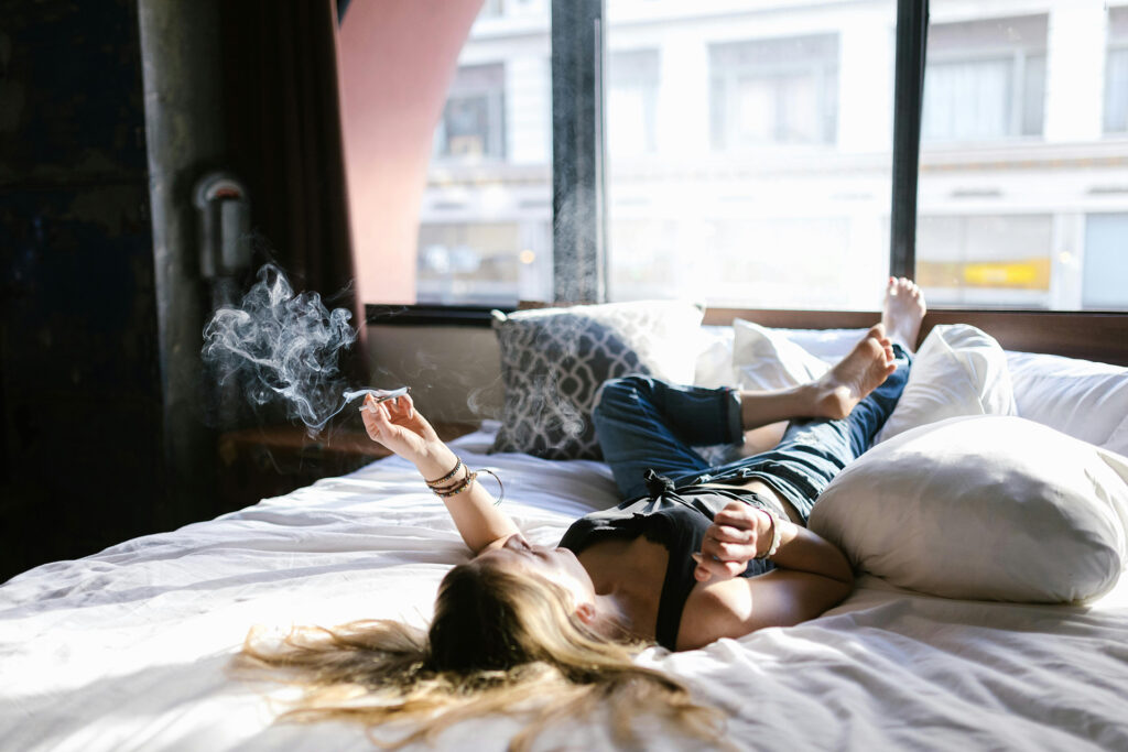 Woman lies on bed with lit joint, relaxing