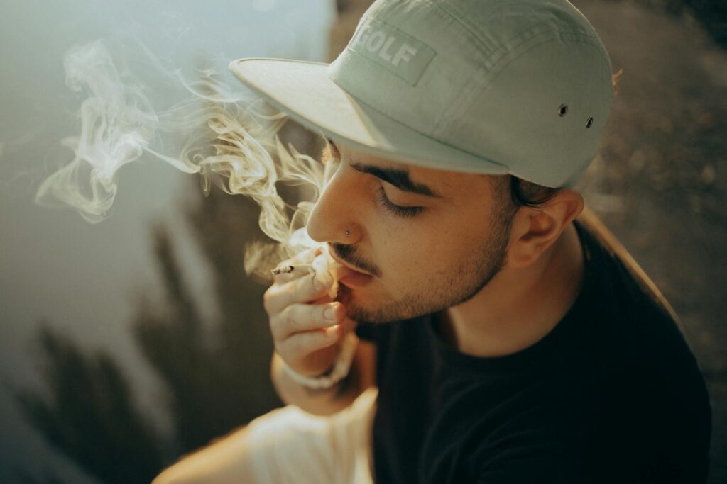 Man wearing a baseball hat smoking a joint