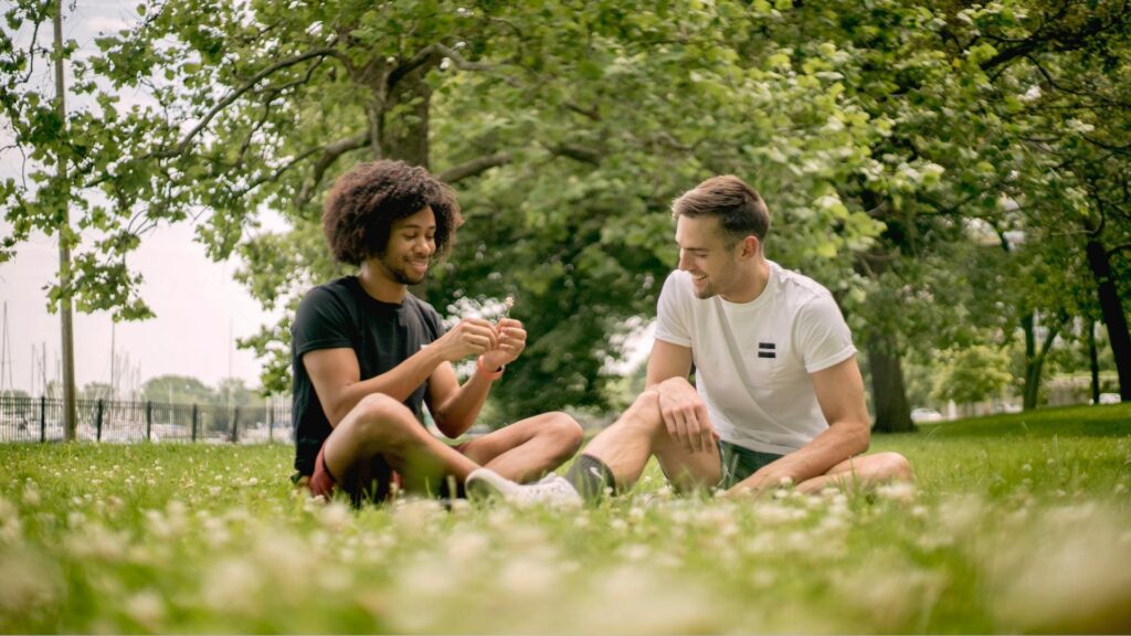 Men Sitting on Green Grass Field lighting a joint