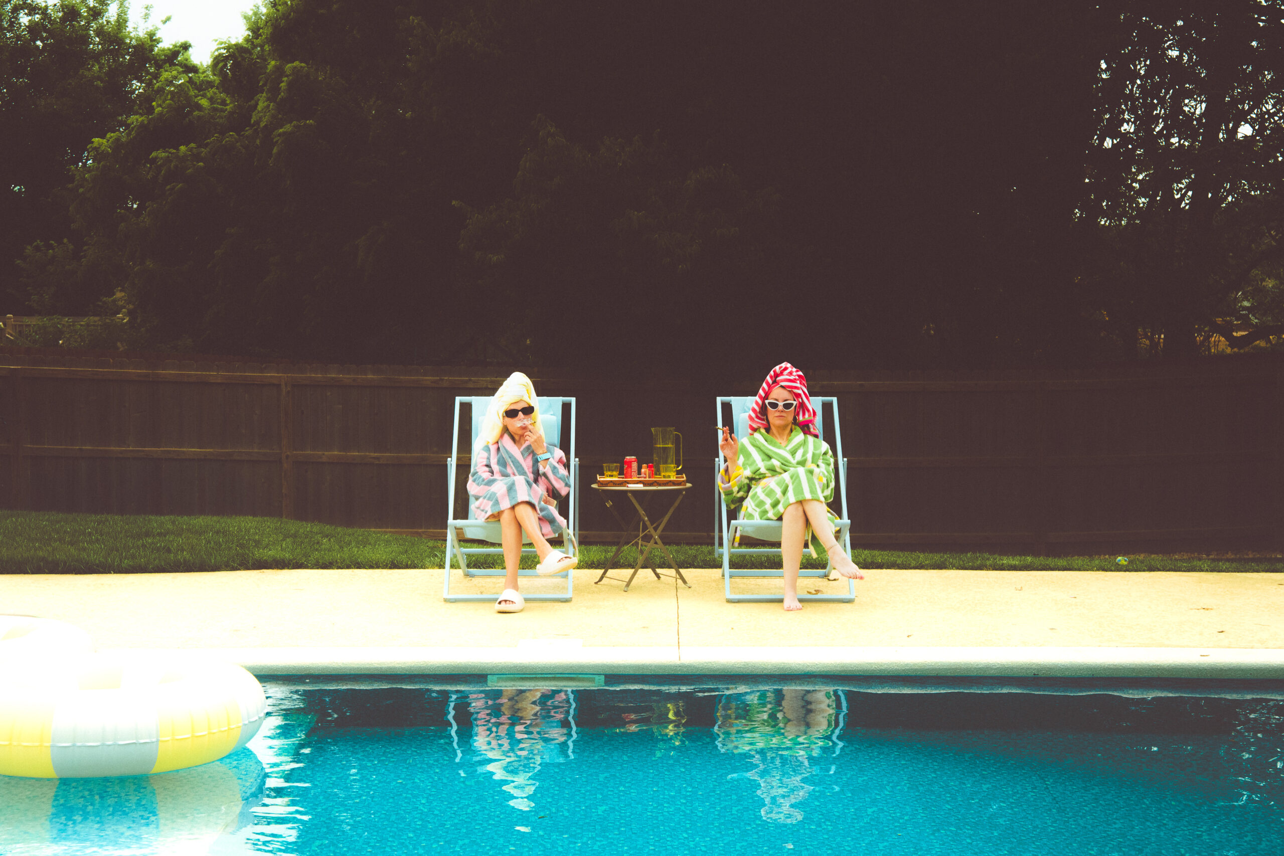 Two people relaxing poolside in lounge chairs, smoking cannabis, on a sunny day.